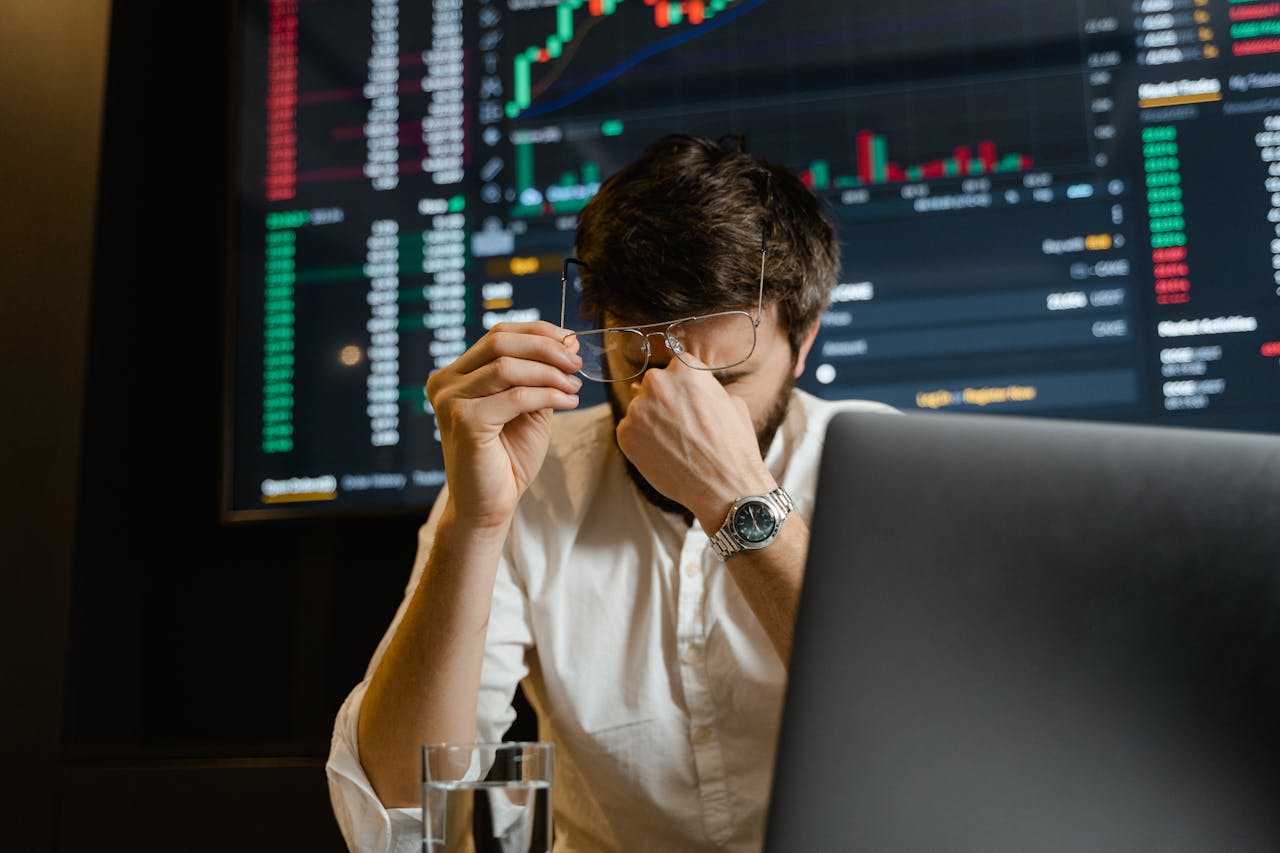 Services-02 A stressed man looks at stock market data on his computer screen in an office setting.